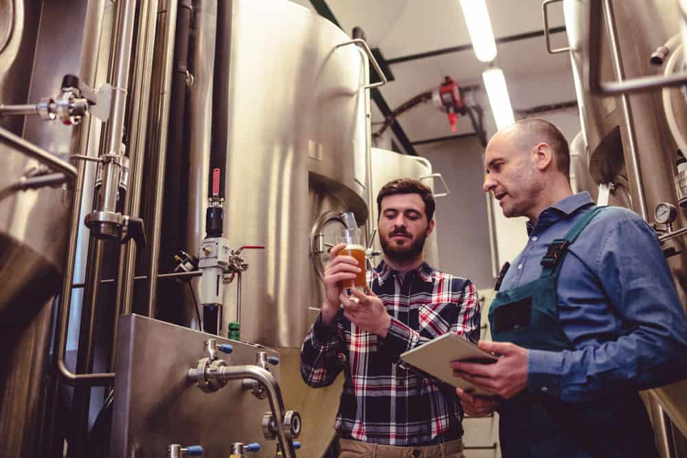 Owner inspecting beer with worker at brewery